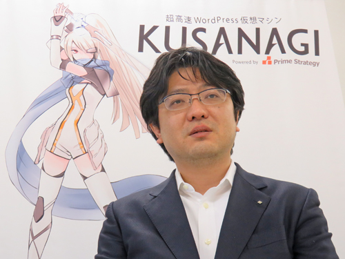 プライム・ストラテジー株式会社 代表取締役 CEO 中村けん牛氏。後ろは同社が開発するWordPress仮想マシン「KUSANAGI」の壁掛け
